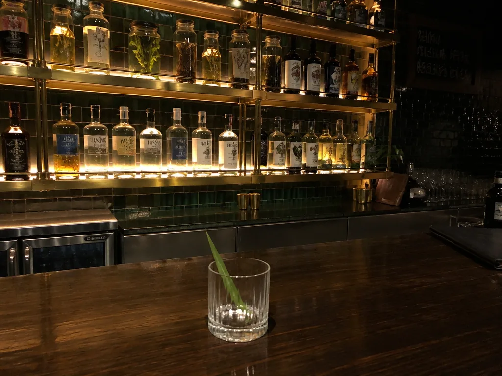 Underground craft cocktail bar with low amber lighting, brass bar shelves, and a lowball glass
