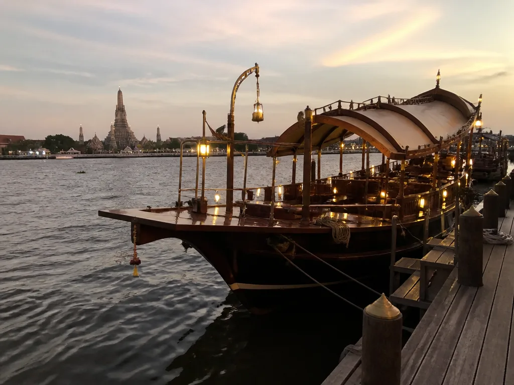Restored teak rice barge moored at Chao Phraya river pier at dusk