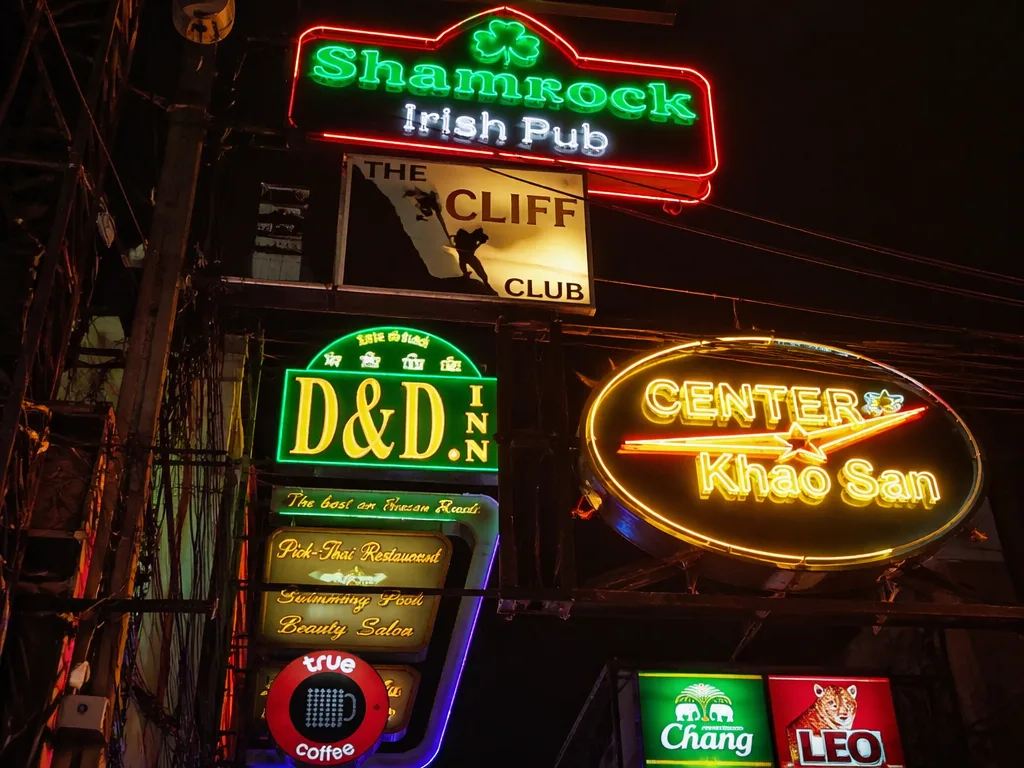 Dense neon bar signs and tangled overhead cables along Khao San Road at night