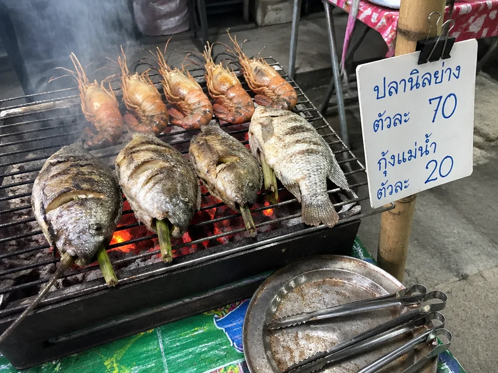 タイ市場の屋台の炭火グリル 、 丸ごとティラピアと大きな海老が煙を上げて焼ける様子