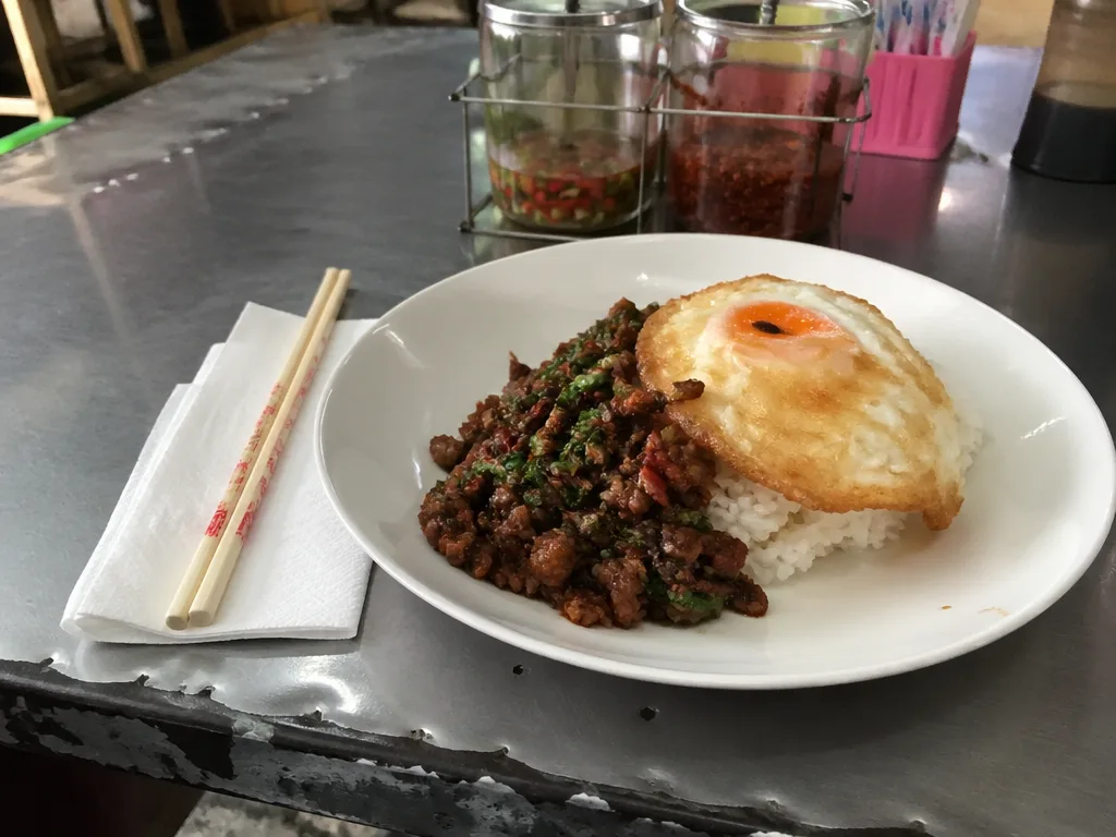 Plate of pad kra pao with fried egg on Bangkok hawker table