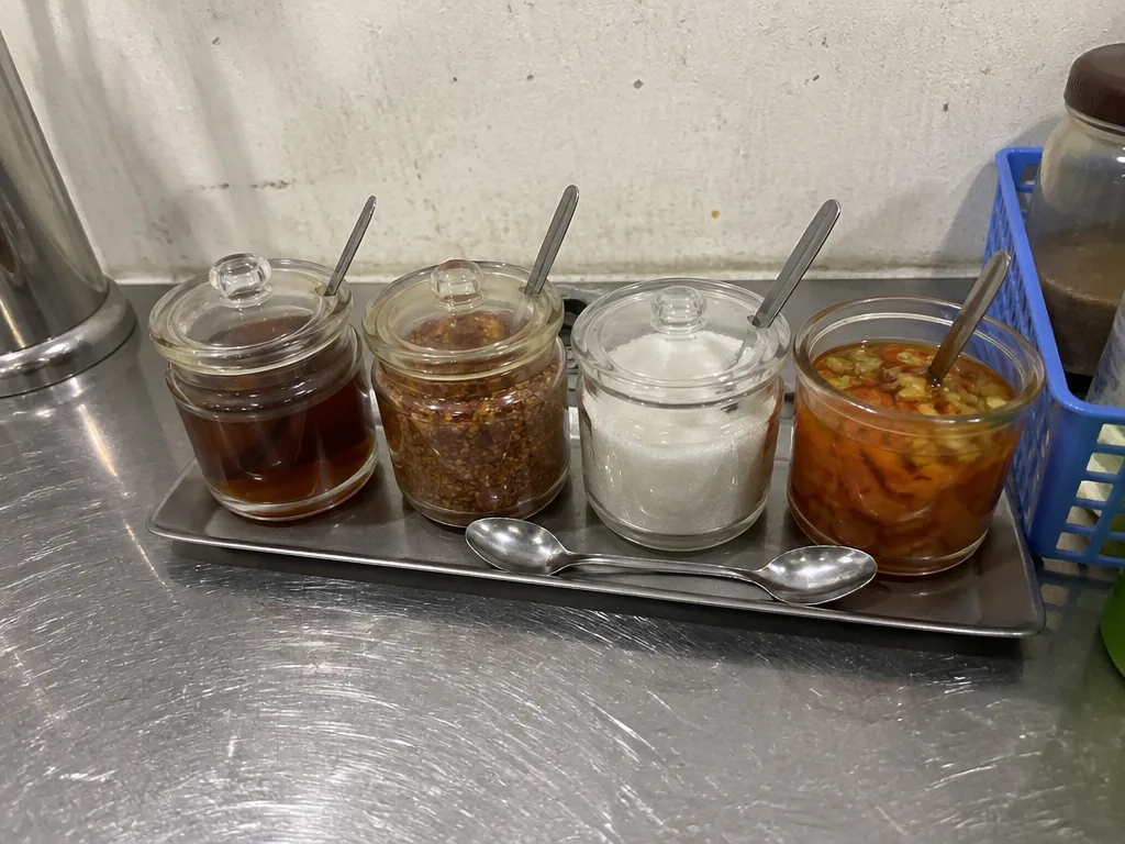 Noodle stall condiment station with fish sauce and chili flakes