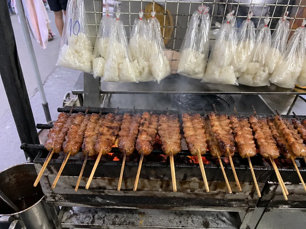 Grilled pork moo ping skewers stacked on a charcoal grill