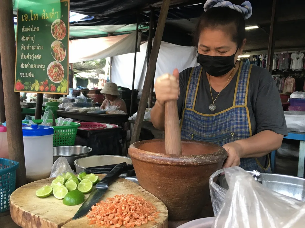 Vendor pounding green papaya salad in a clay mortar