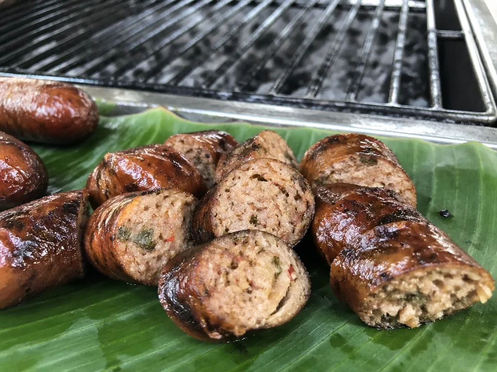 Sliced sai ua northern Thai herbal sausage on a banana leaf with charcoal grill behind