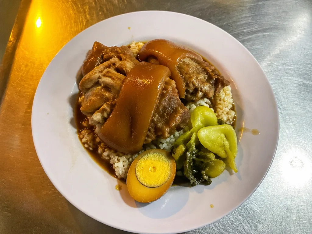Plate of khao kha moo stewed pork leg over rice with boiled egg and pickled greens