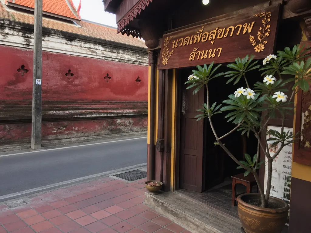 Quiet shophouse massage entrance with hand-painted Lanna sign near a Chiang Mai temple wall