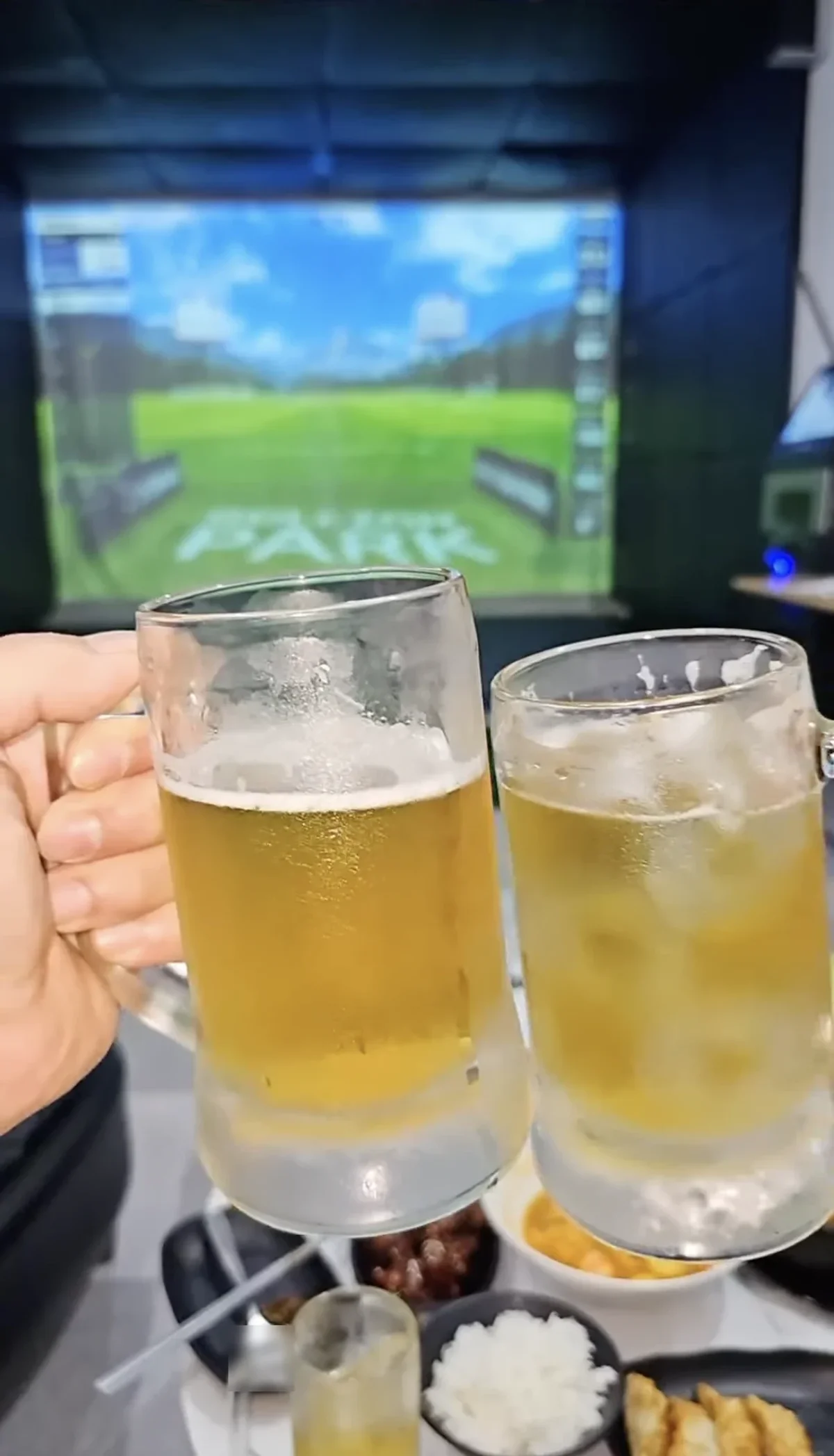 Two beer mugs toasting in front of the screen golf display