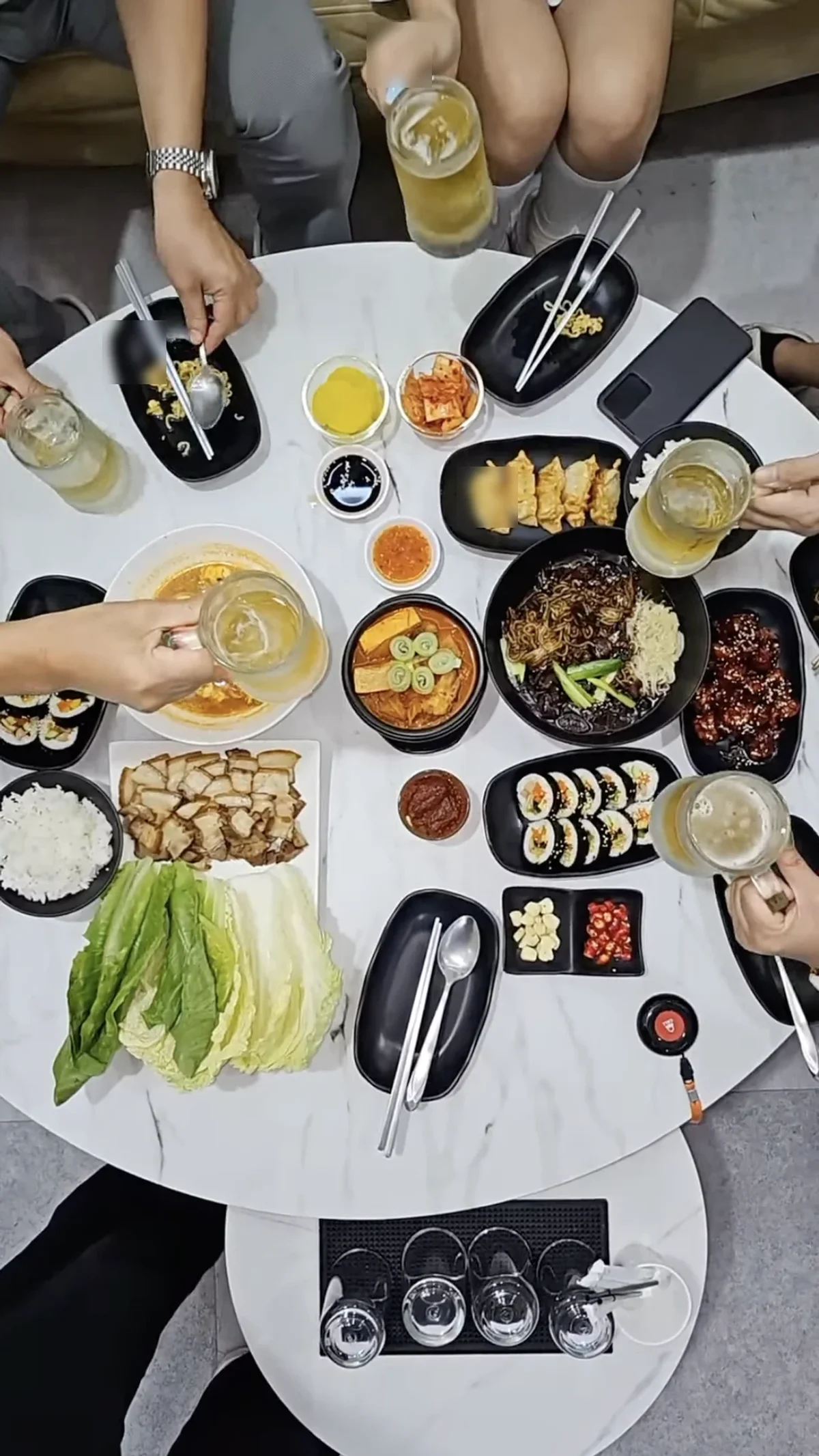 Overhead spread of Korean dishes with beers being toasted
