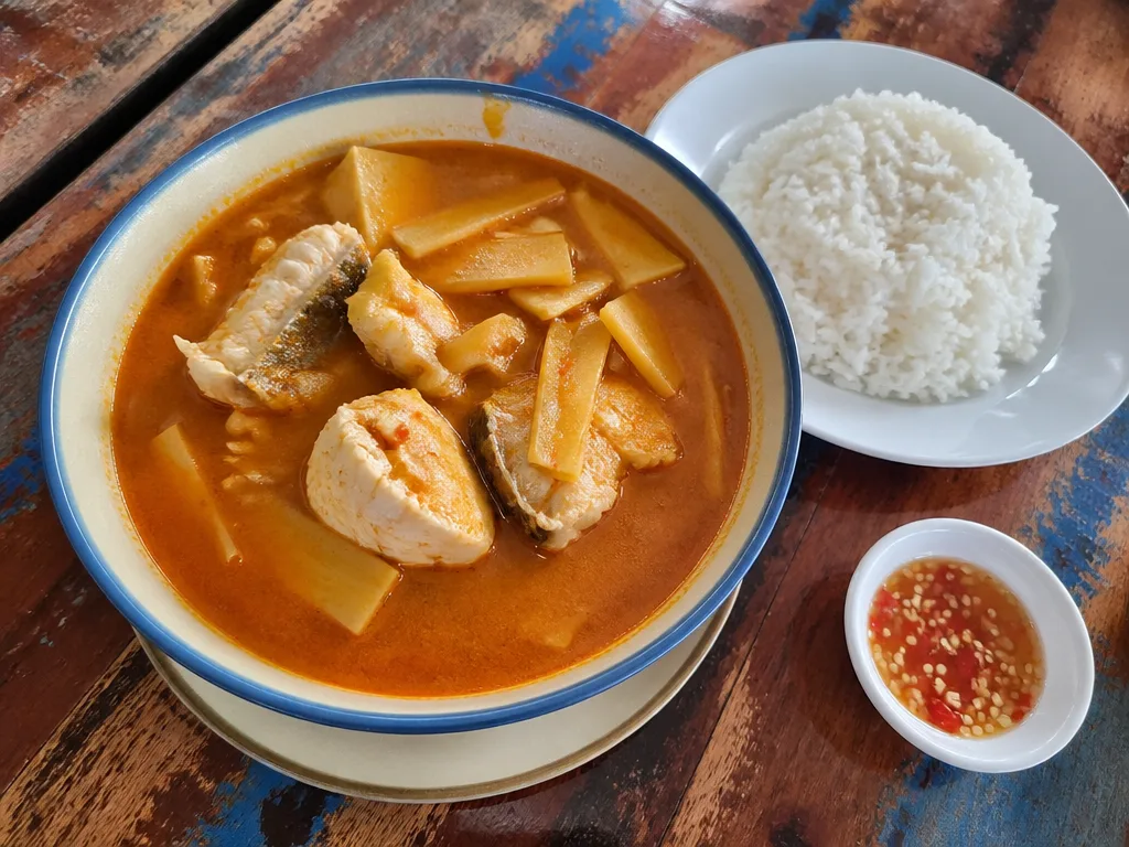 Bowl of southern Thai sour curry kaeng som with fish and vegetables at a shophouse table