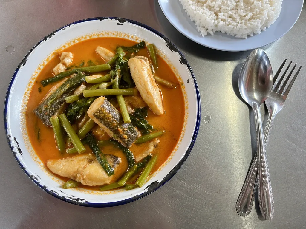 Bowl of southern Thai kaeng som sour curry with sea bass and morning glory next to steamed rice