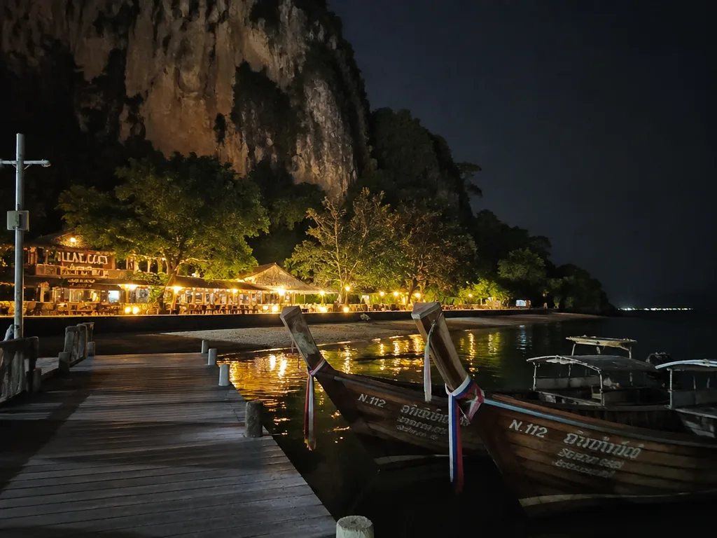 Longtail boats moored at Railay East pier with bar lights glowing onshore