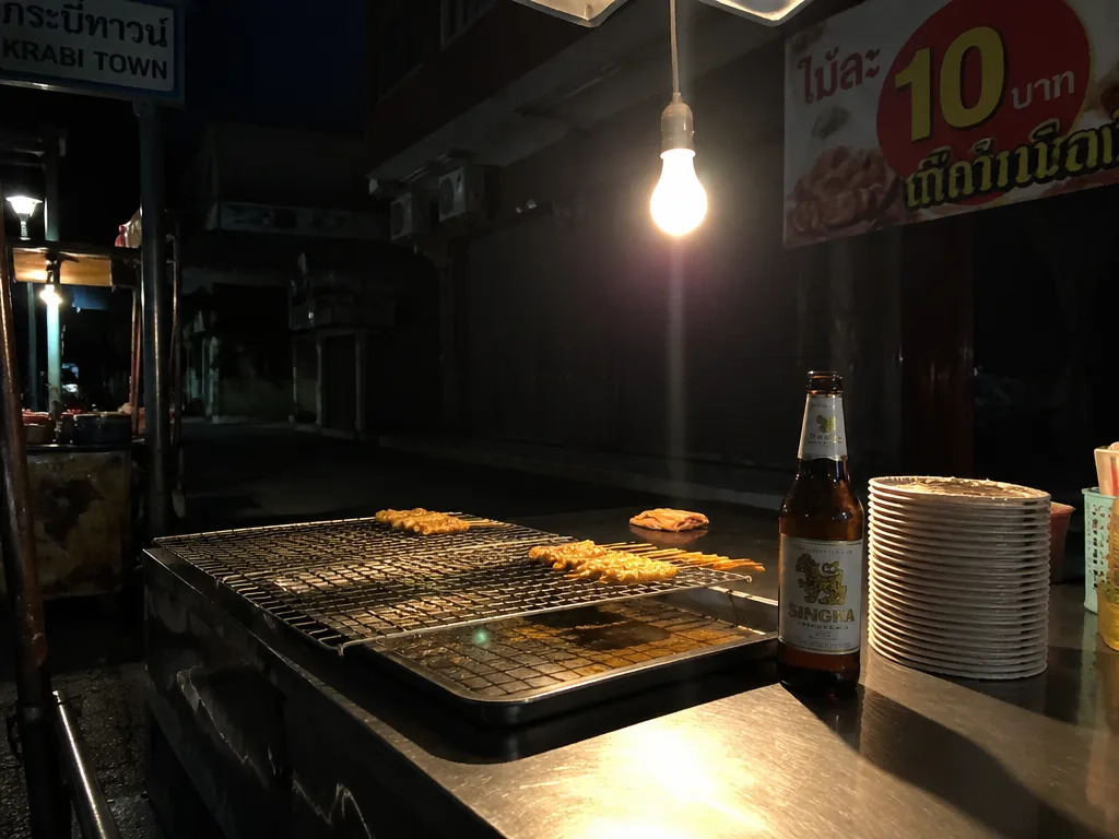 Krabi Town night market food stall with hanging bulb and skewers cooling on the grill
