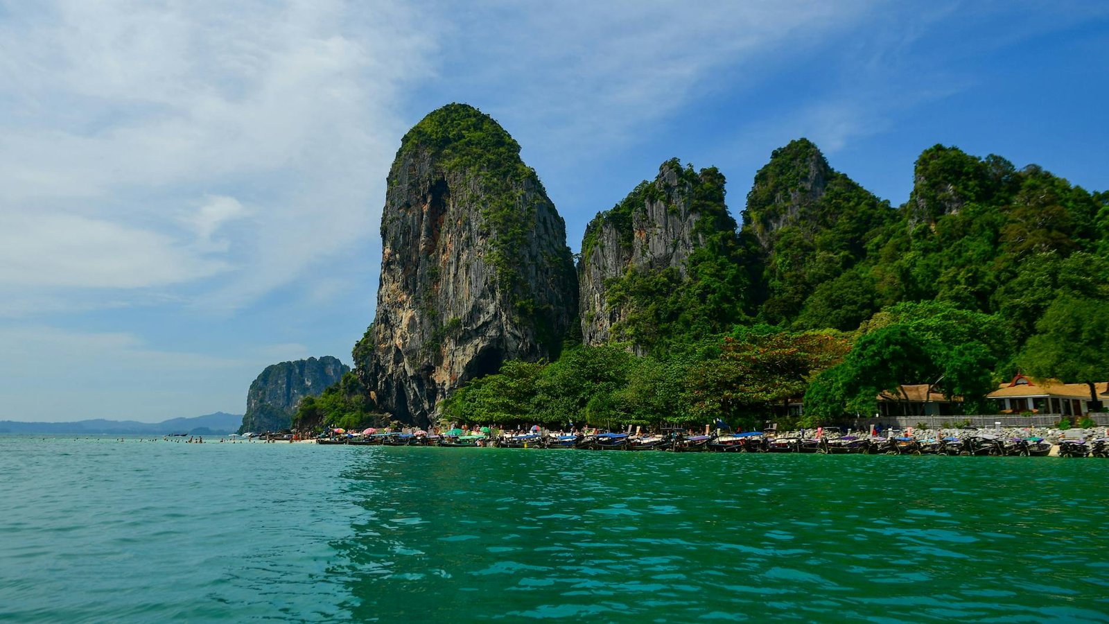 Krabi limestone karsts rising from turquoise water with longtail boats on the beach
