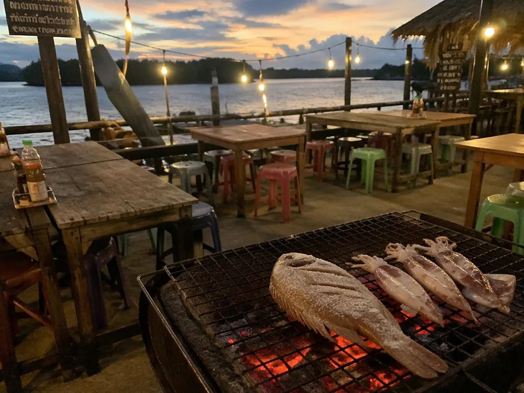 Fresh whole fish on charcoal grill at Krabi Town riverfront restaurant at dusk