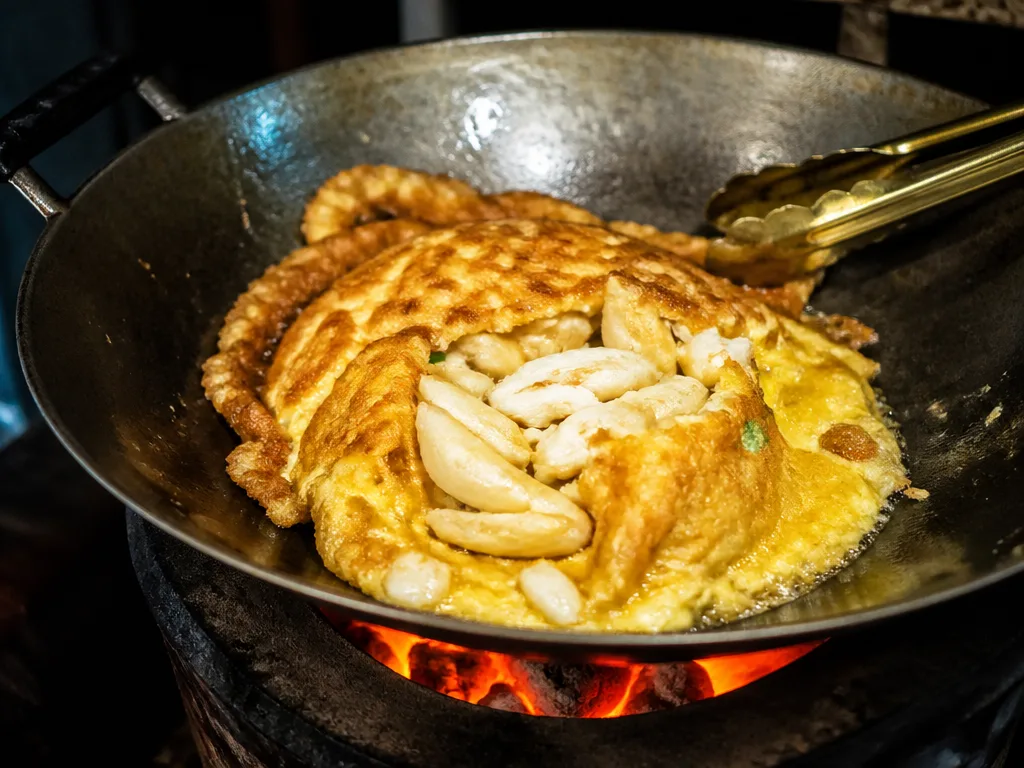Crab omelette being cooked over charcoal flames at a famous Bangkok street stall