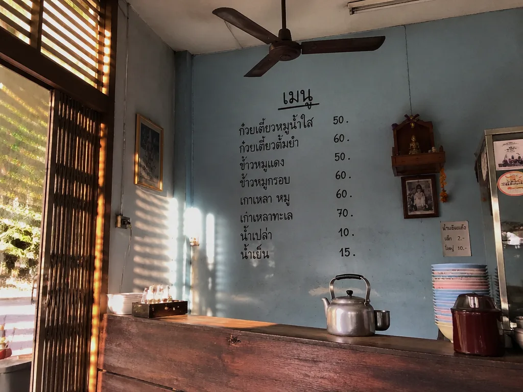 Quiet Sukhumvit shophouse food stall with handwritten Thai menu on the wall