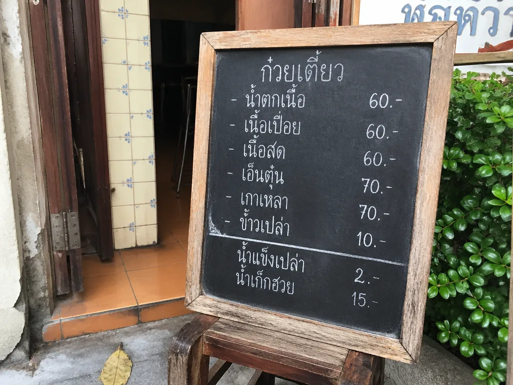 Handwritten Thai script chalkboard menu outside Bangkok noodle shop