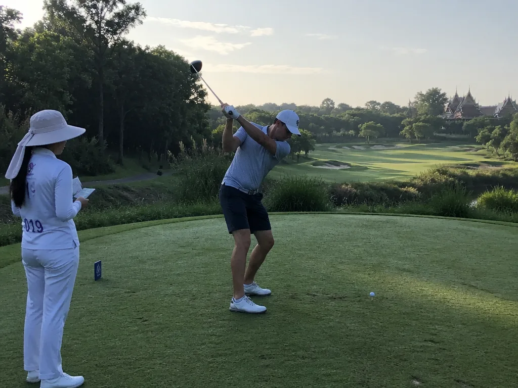 Golfer teeing off at a Thai golf course with caddie standing nearby