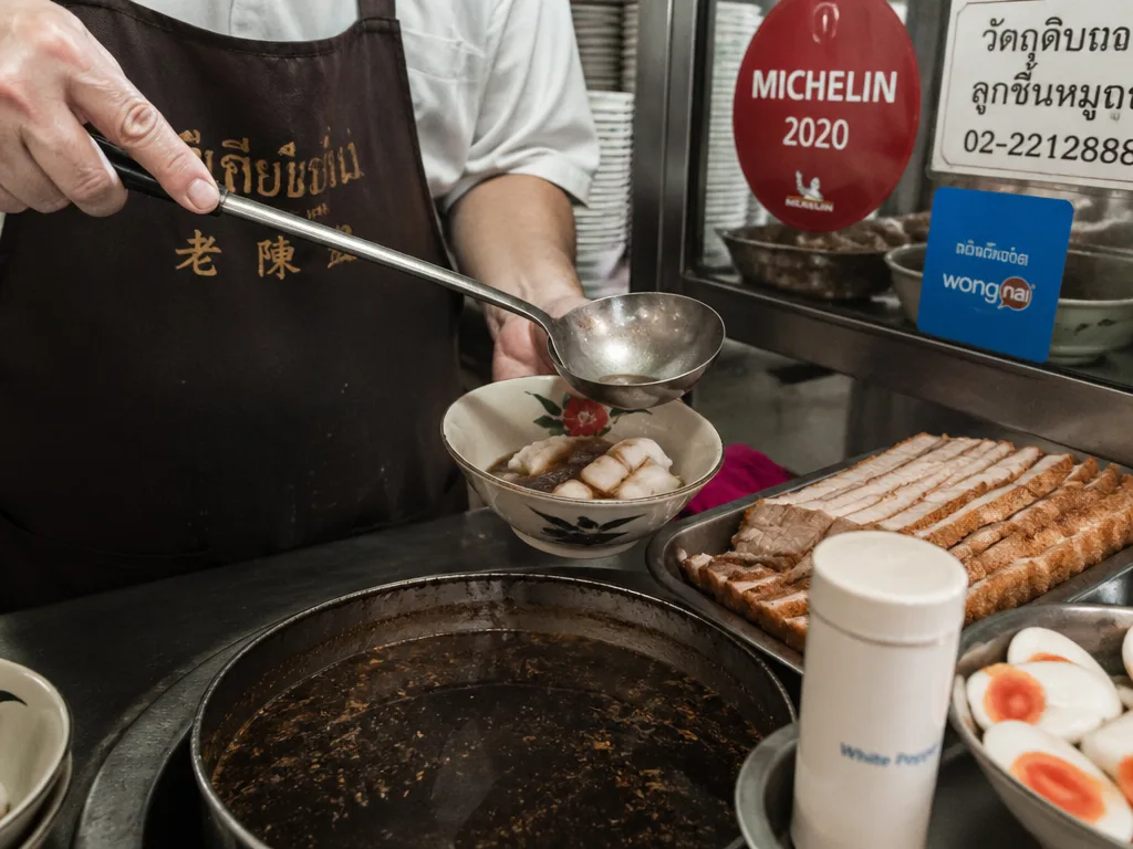Vendor ladling rolled rice noodle soup into ceramic bowl