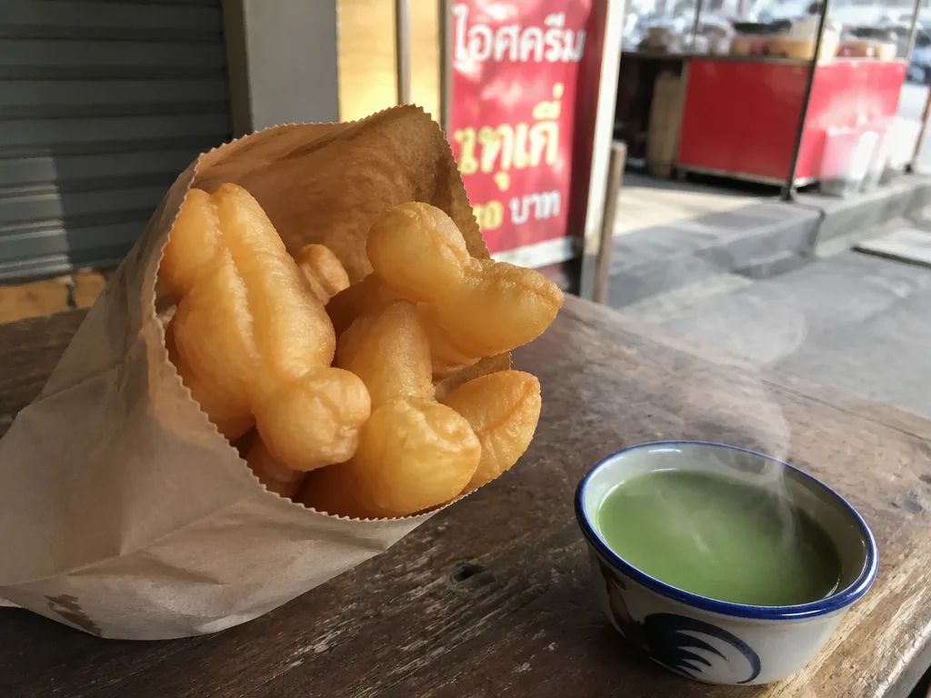 Crispy Thai doughnuts beside hot pandan custard cup